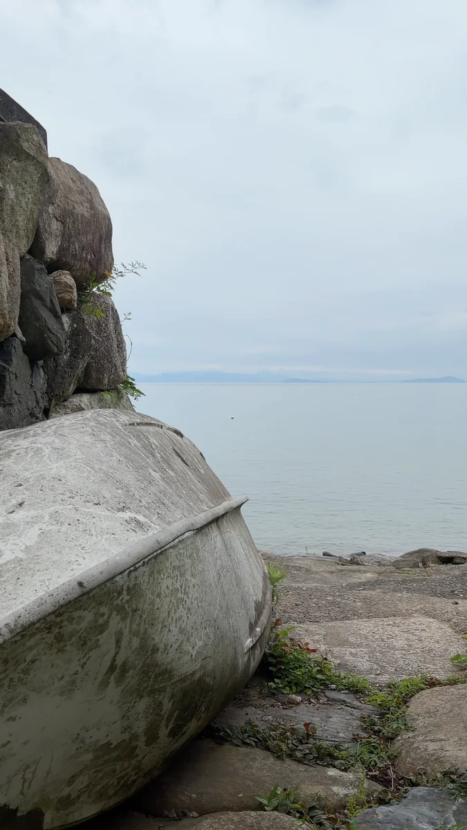 (左)蔵の脇の小道。抜けた先が湖岸です/(右)石積みの上に伏せられた小舟と、琵琶湖。対岸の山まで見えます