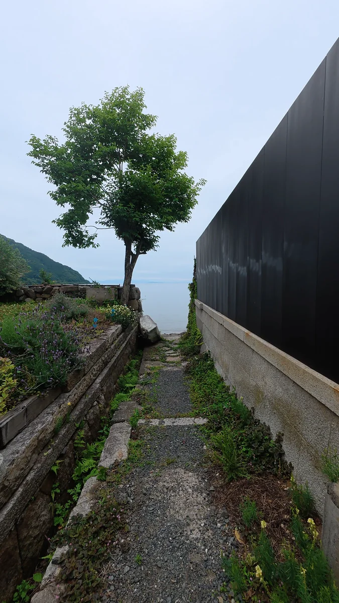 (左)蔵の脇の小道。抜けた先が湖岸です/(右)石積みの上に伏せられた小舟と、琵琶湖。対岸の山まで見えます
