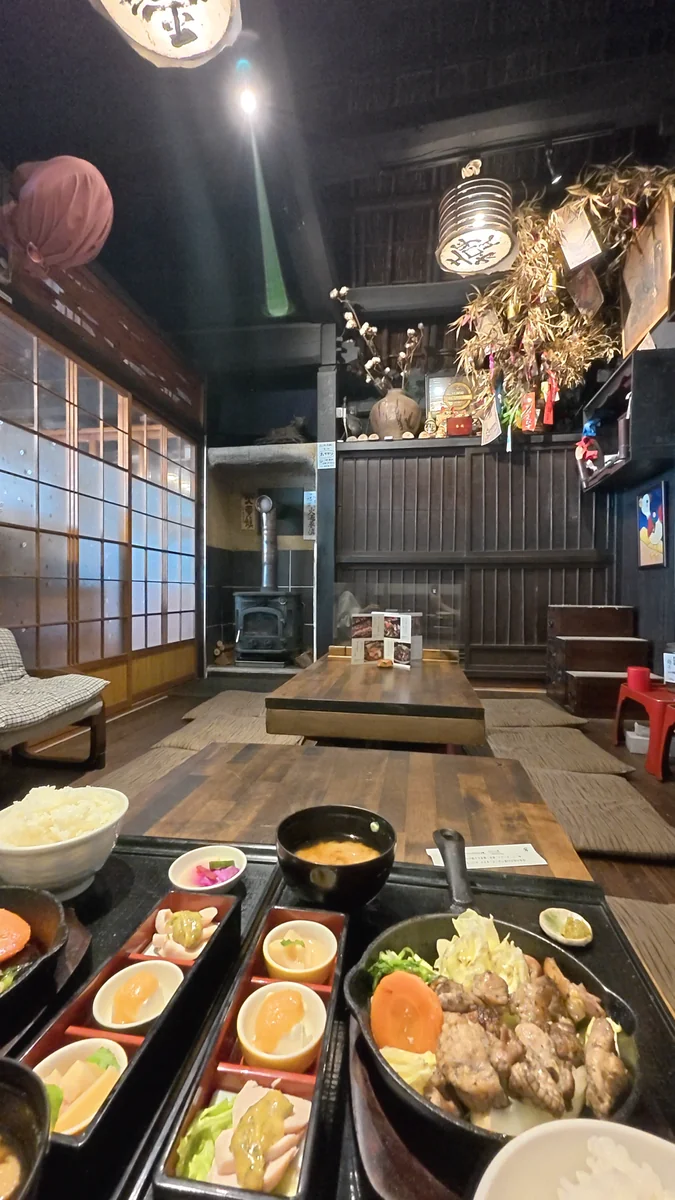 座敷。低い座卓が並び、奥に薪ストーブがあります。柱と梁は黒いまま